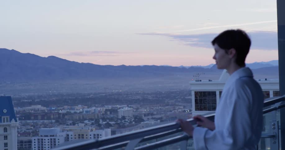 A woman wearing a bathrobe walks out onto the balcony