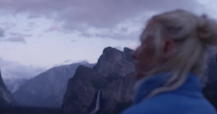 A blond haired woman looks around at the mountains