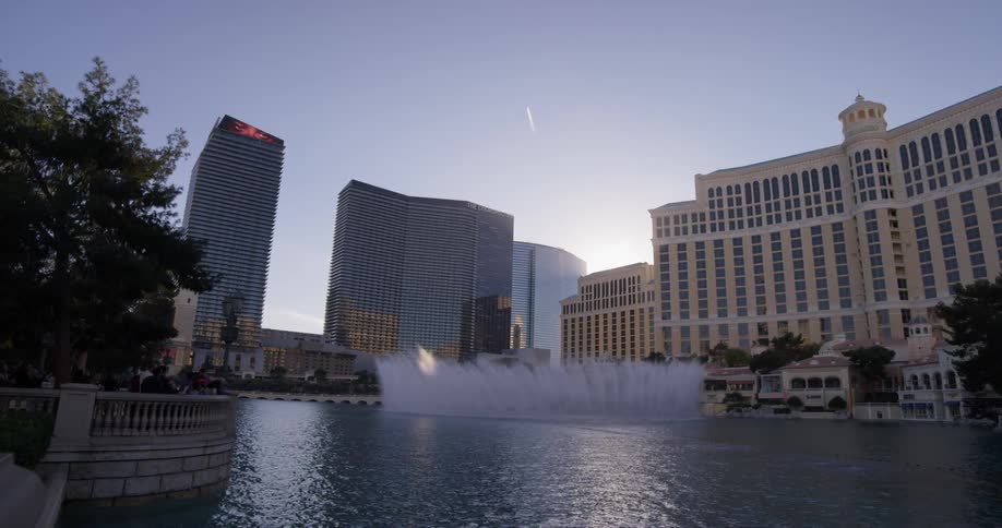 Fountains spray up in front of a large hotel at sunrise