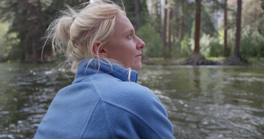 A woman looks around smiling by the stream