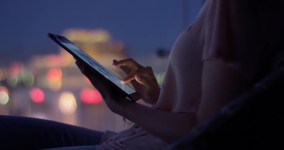 A woman uses a tablet in a city at night