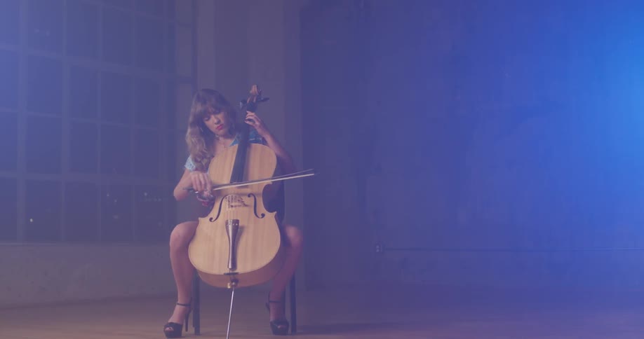 A woman plays a cello in a dim room