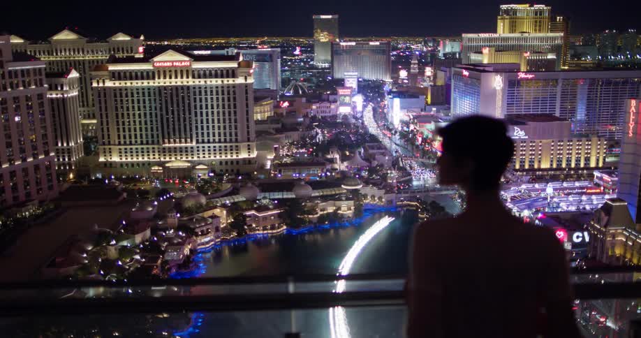 A woman watches over the city at night from her balcony