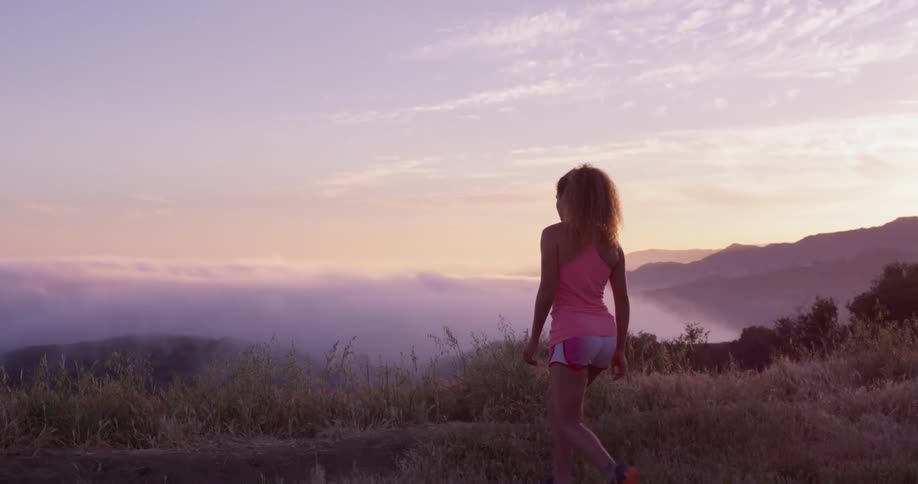 Woman is walking towards mountain lookout at sunset