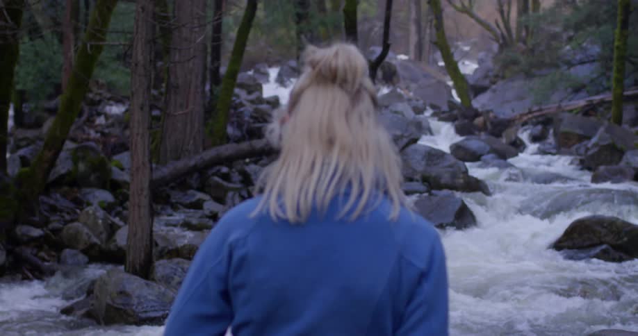 A woman stands next to a river in a forest
