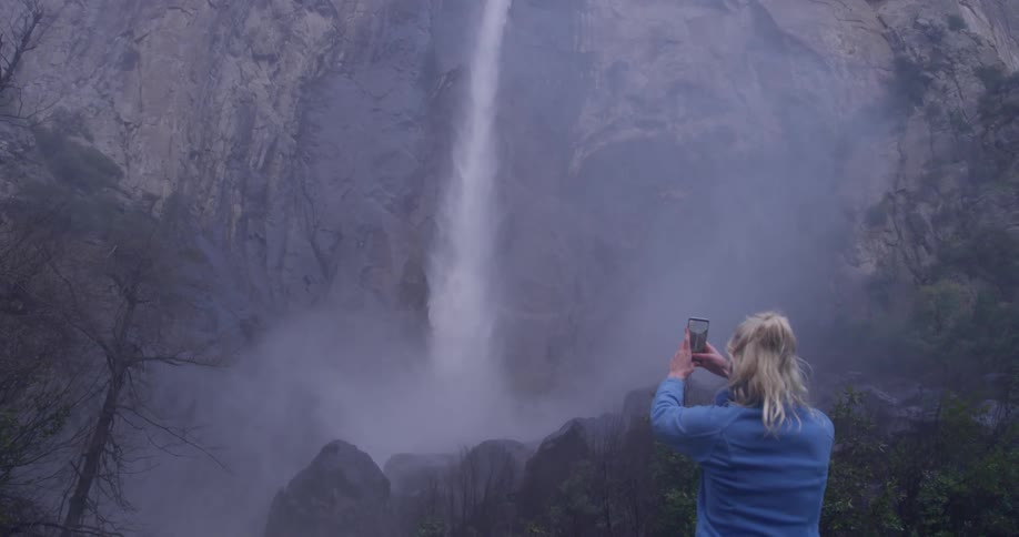 Woman takes a picture of a large waterfall with her phone