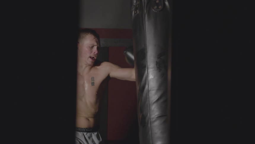 A man wearing boxing gloves punches and kicks  a large punching bag in a gym