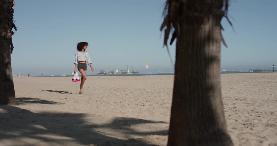 A woman carries skates on a sandy beach