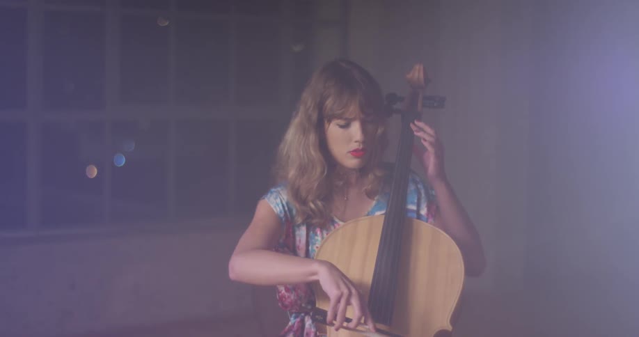 A woman plays a cello in a dim room