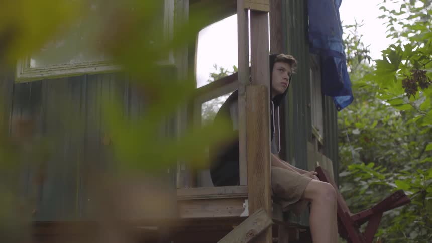 A boy sits on the edge of a tree house