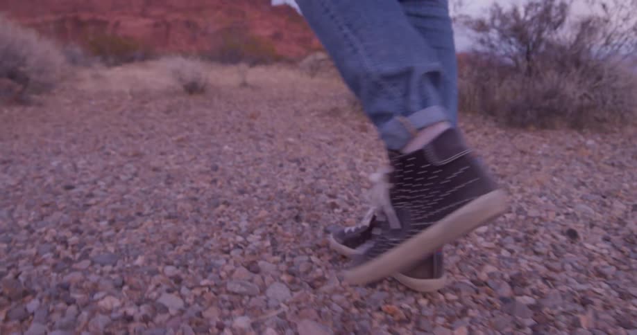 Woman wearing brown shoes walks over the stone covered trail