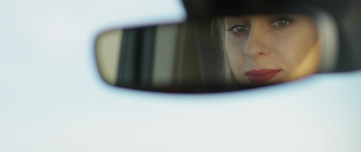 A woman is reflected in a rear view mirror while driving a car
