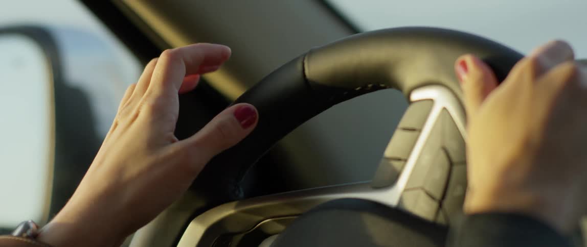 A woman's hands turn a car steering wheel on a sunny day