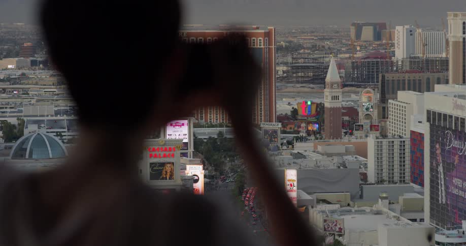 A woman takes a picture of las vegas from a hotel balcony