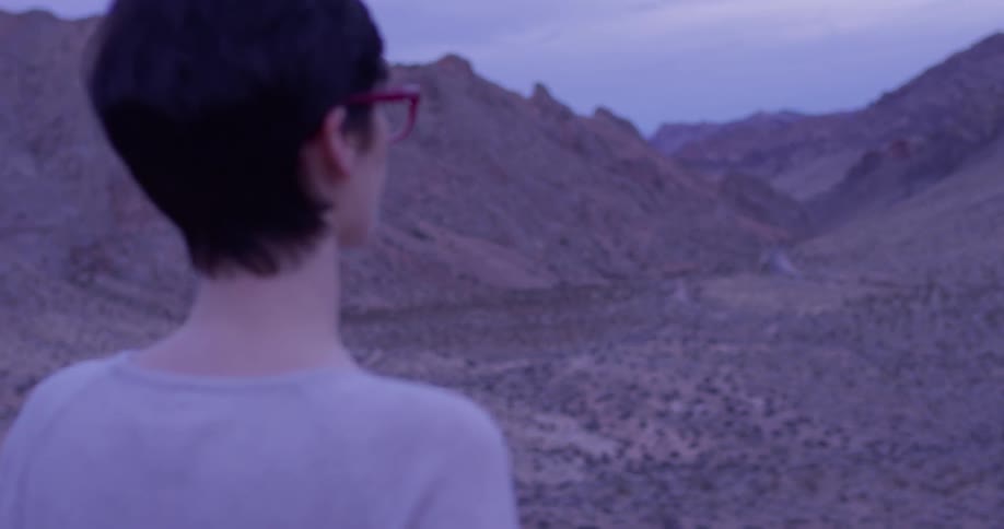 Woman wearing glasses looks out at the hills under a cloudy sky