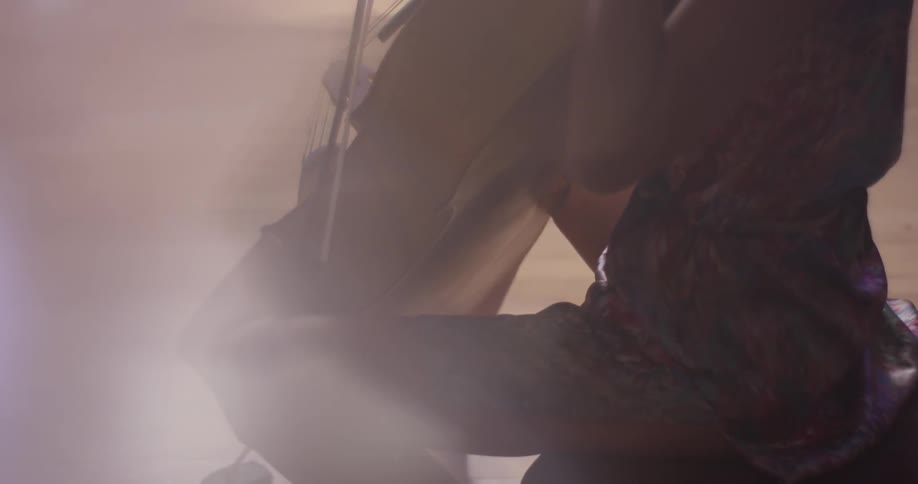 Woman drags a bow across the strings of a cello
