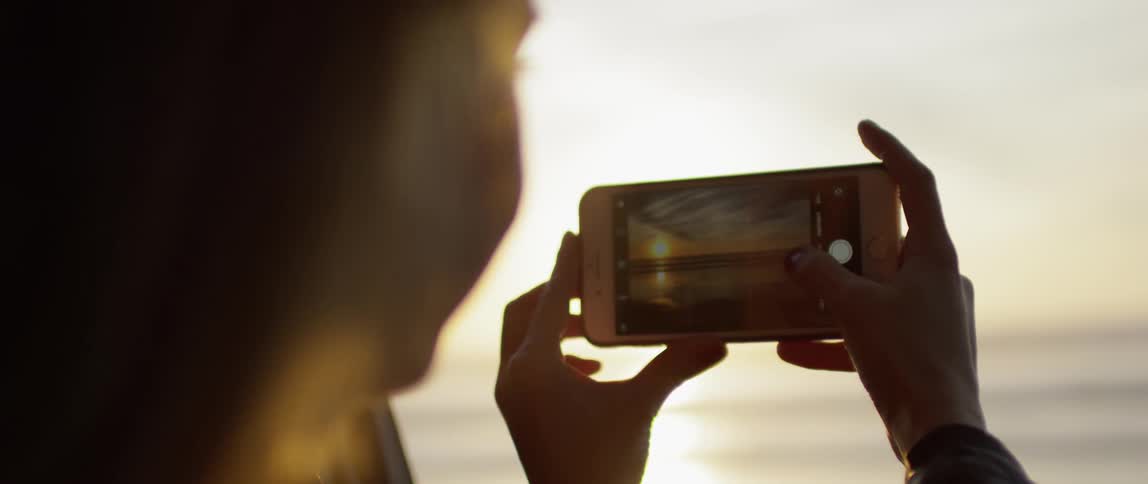 A woman holding up her phone photographs the sunset