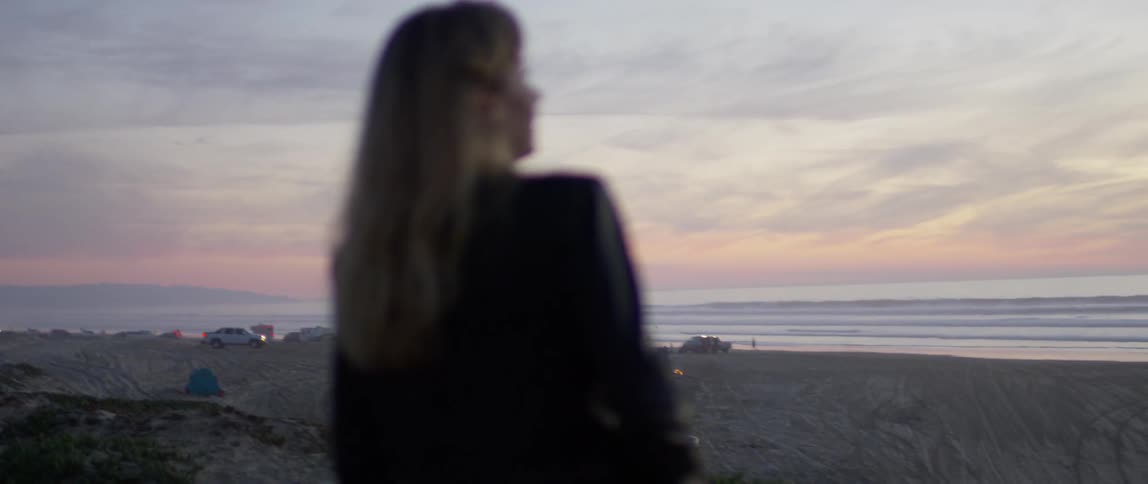 Woman looks at vehicles parked on the beach at sunset