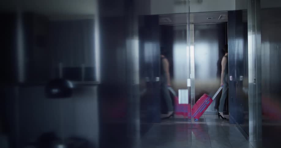 Woman walks down the hallway of an office building pulling a suitcase