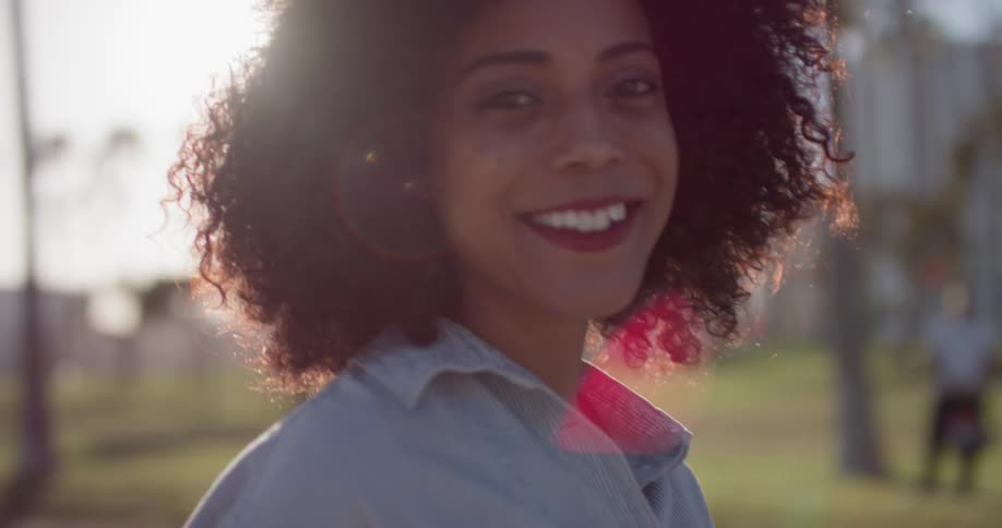 A woman stands outside in the sunshine and smiles and poses