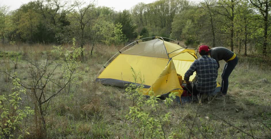 A man and woman sit up a tent in the woods