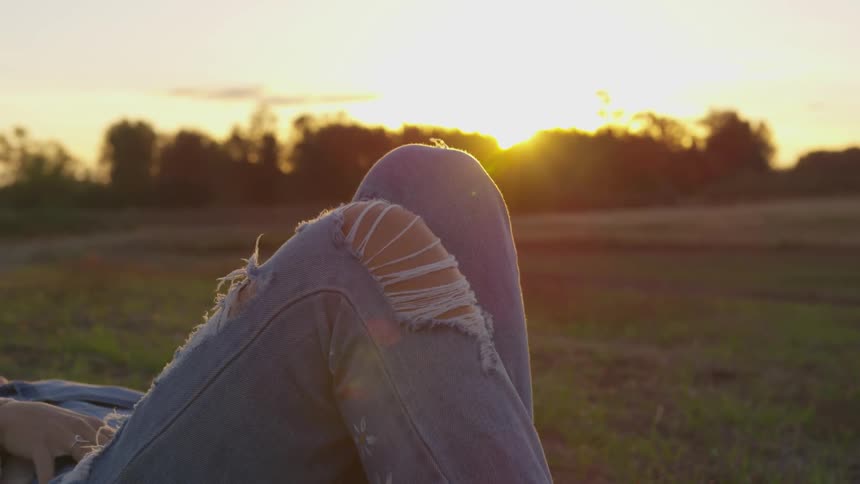 A woman lies in a rural field at sunset