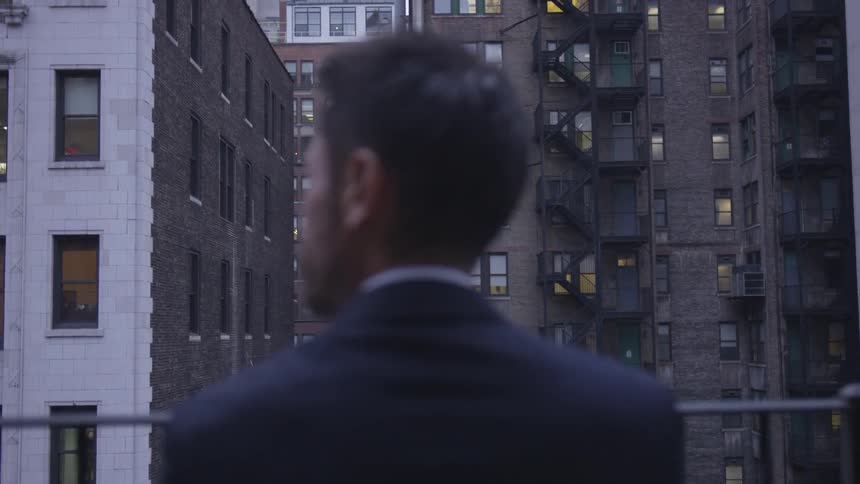 A businessman stands on a balcony in a city