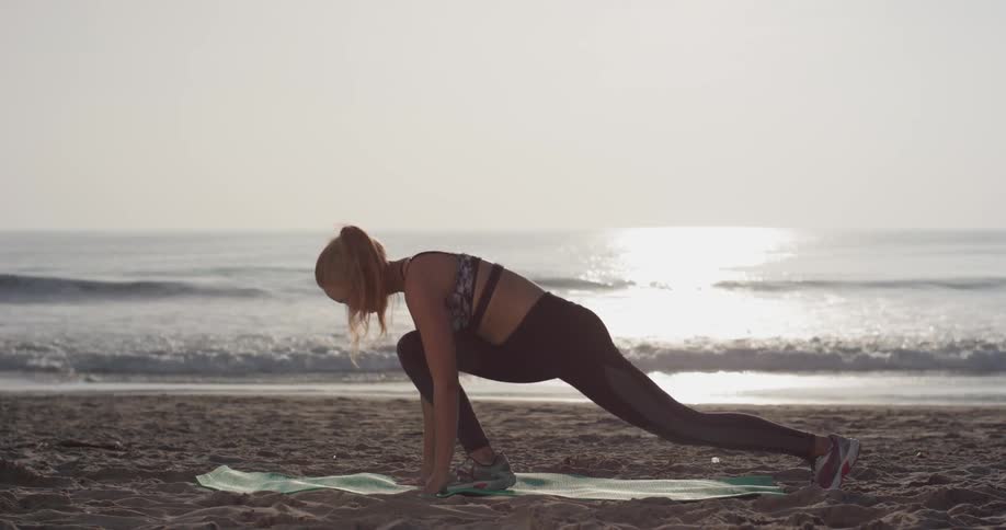 Woman does yoga poses on her yoga mat on the beach