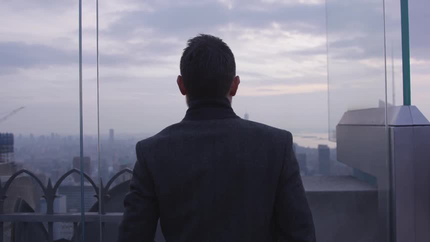 A man looks out at a city at sunset