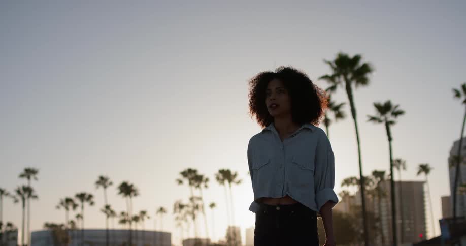 A woman stands outside near palm trees