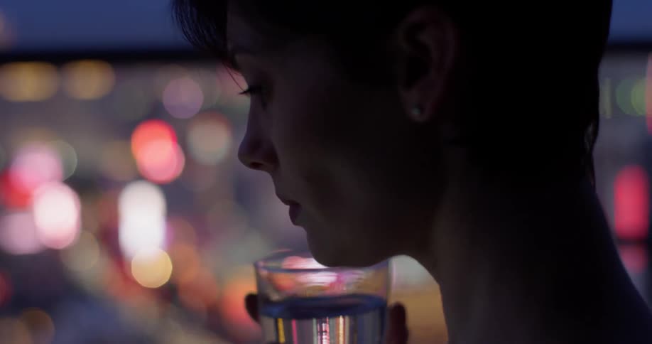 Woman sips out of a glass looking at city lights at night