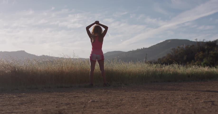 Woman stands in the country on a sunny day stretching her arms