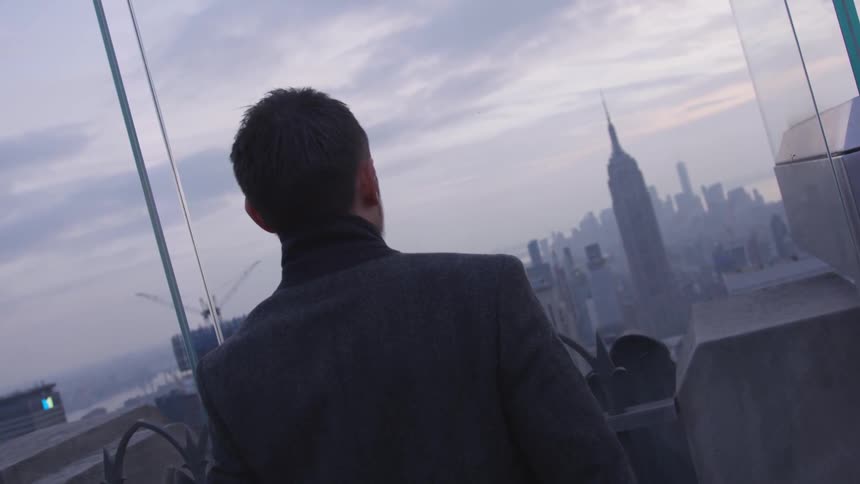 A man looks out at a city at sunset
