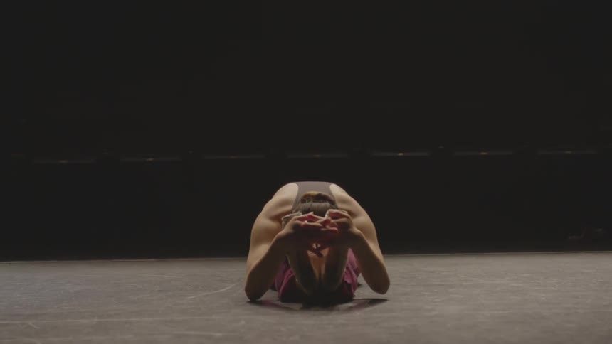 A ballerina stretches over her legs and holds her feet