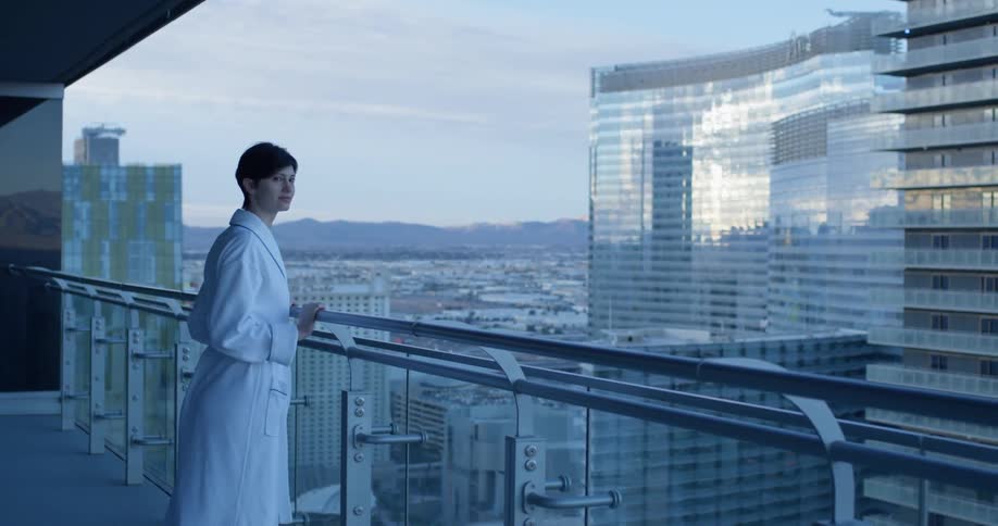 Woman walks onto the balcony and looks out at the city