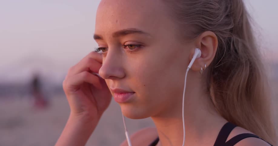Young woman places earbuds in her ears then closes her eyes