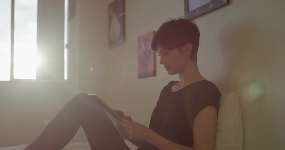 A woman sits in bed using her tablet