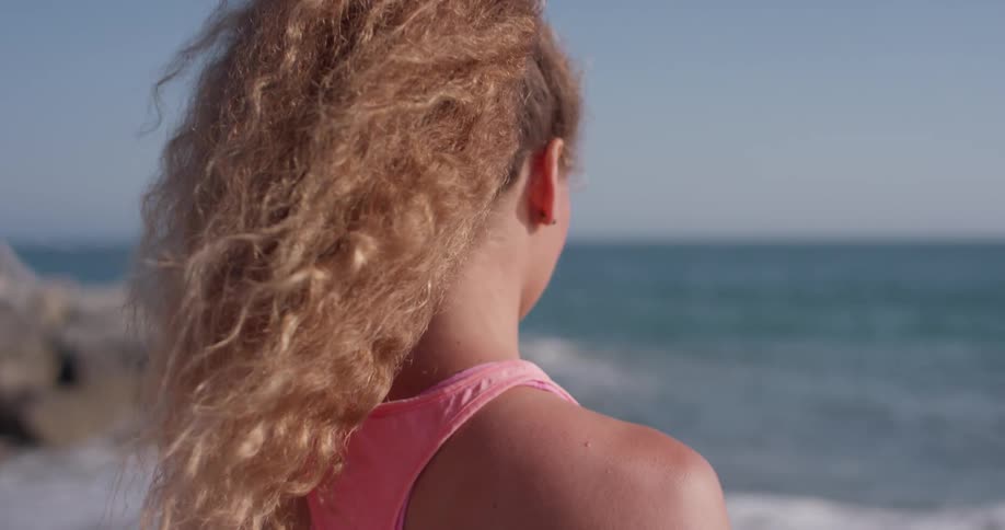 A woman stands on the beach by the water