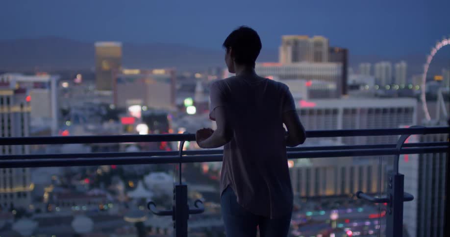 Woman leans against a balcony looking out at a city