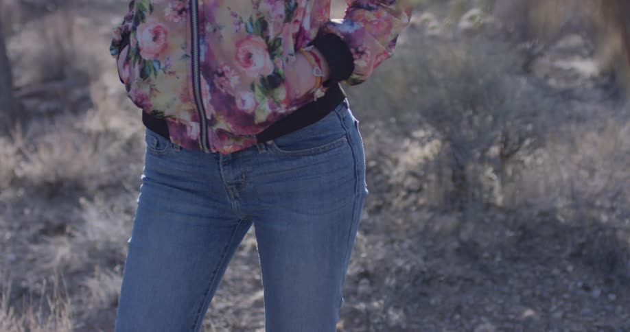 A woman stands next to a plant in a desert