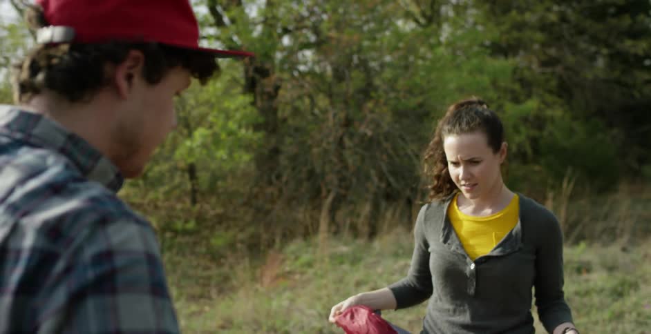 A man and woman talk as they fold up some camping equipment