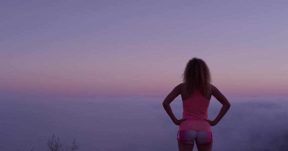 Sun sets behind hills as a woman looks out over the clouds