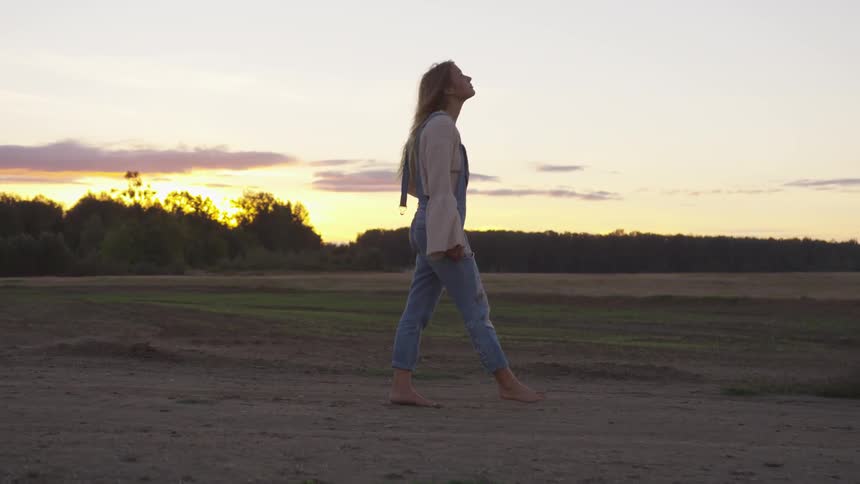 A woman is walking on the field slowly at sunset