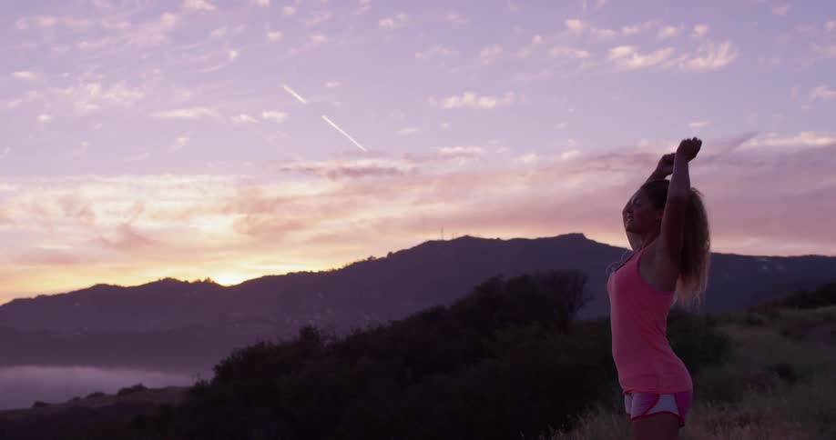 A woman stretches her arms out from atop a hill