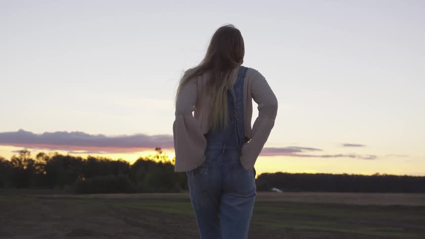 Woman puts her hands in her back pockets as she stands in a field