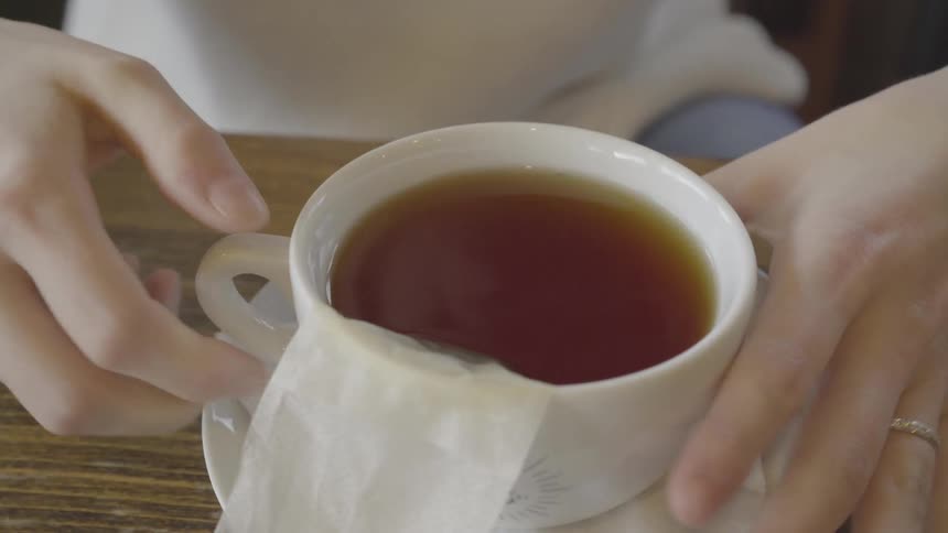 A person is setting their cup of tea down on a saucer inside in daylight
