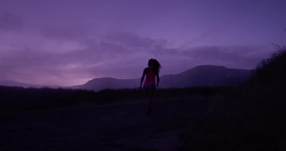 A woman walks on a dirt road at dusk