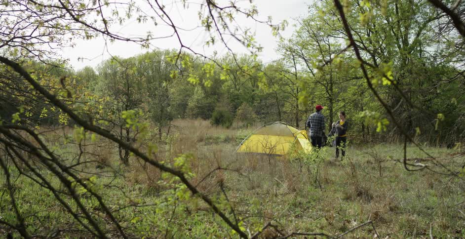 A man and woman are outside in the wilderness by a tent