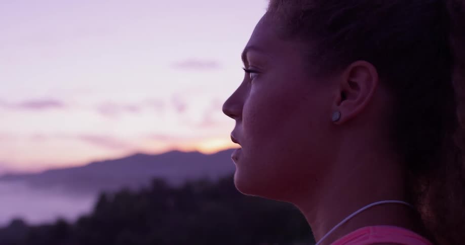 A woman stands on top of a mountain and removes her ear buds