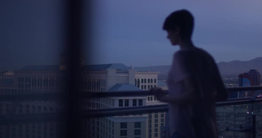 Woman leans on a balcony looking down at the city below